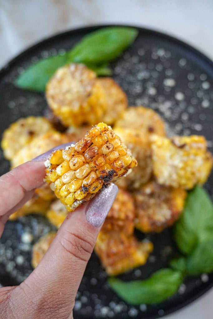 a hand holding a fried corn on the cob above a plate of more