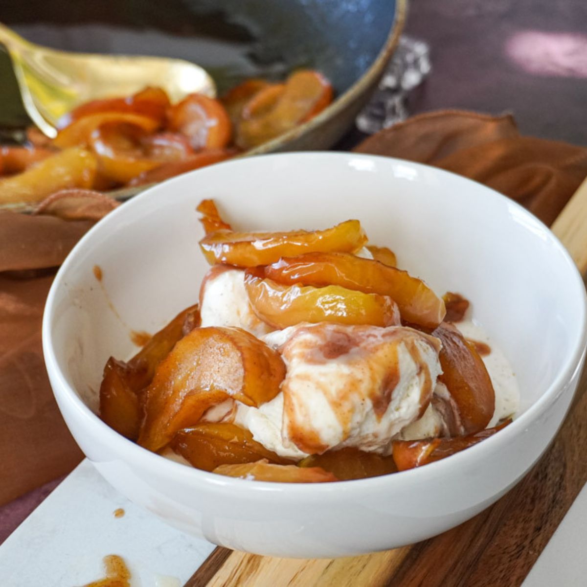 southern fried apples in a white bowl scooped over vanilla ice cream