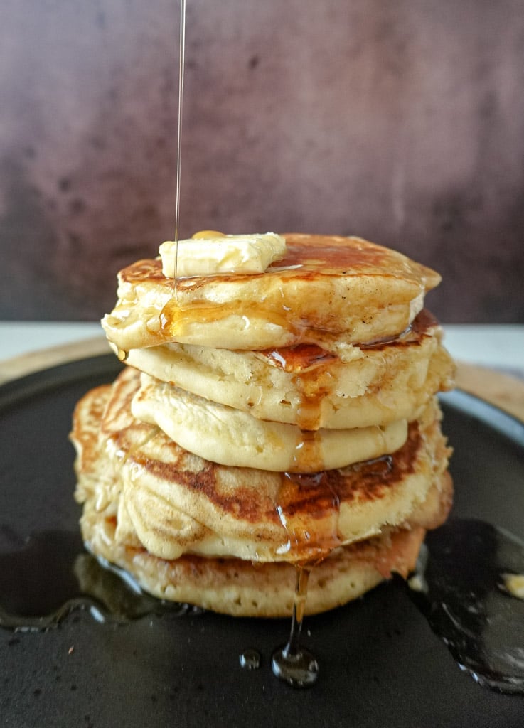 syrup being poured over a stack of old fashioned pancakes