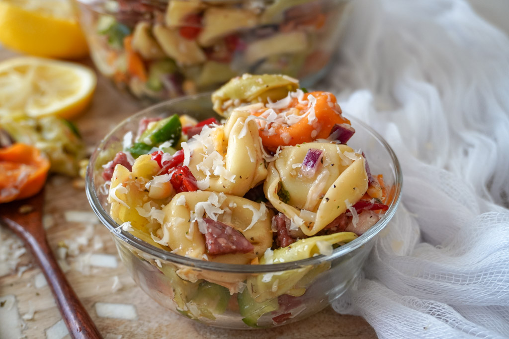 a small bowl of Tortellini Pasta Salad with a larger bowl with more behind it