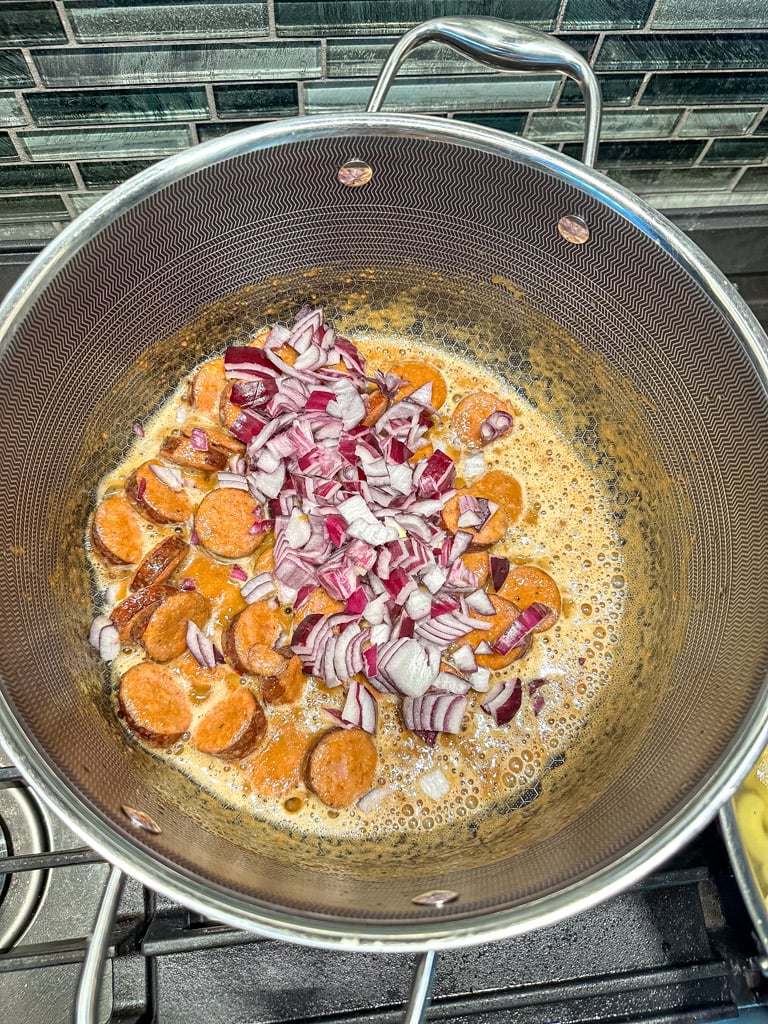 red onions added to a stockpot filled with cooked sausage and seasoning