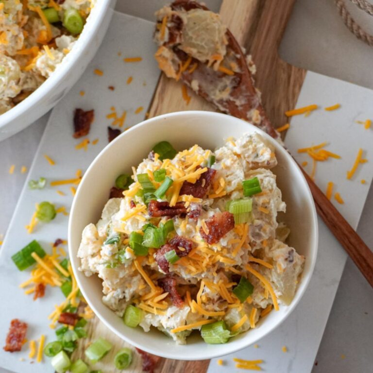 baked potato salad in a small white bowl garnished with cheese and chopped bacon