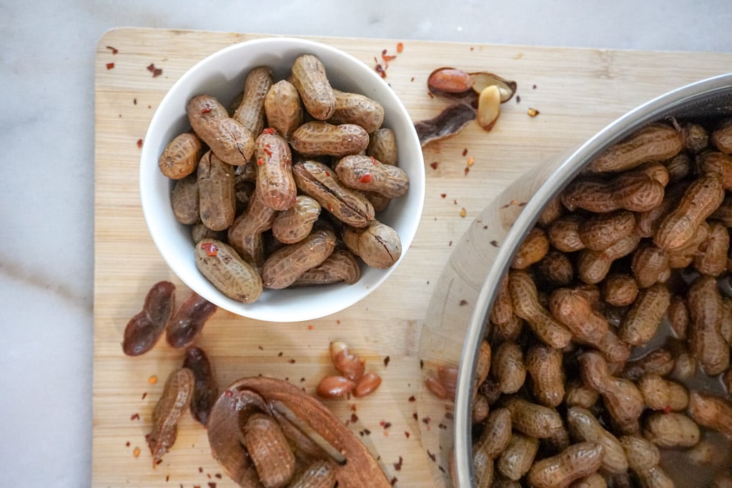 overhead view of cajun boiled peanuts in a bowl with a large pot containing more in the right hand corner