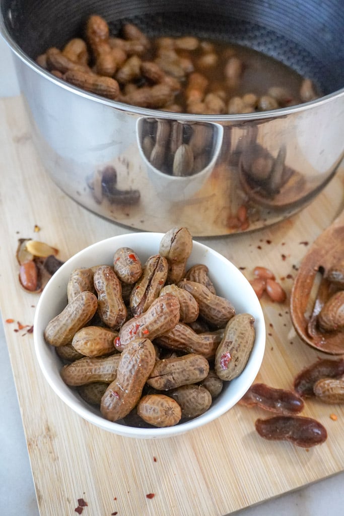 a bowl of cajun boiled peanuts with a pot containing more