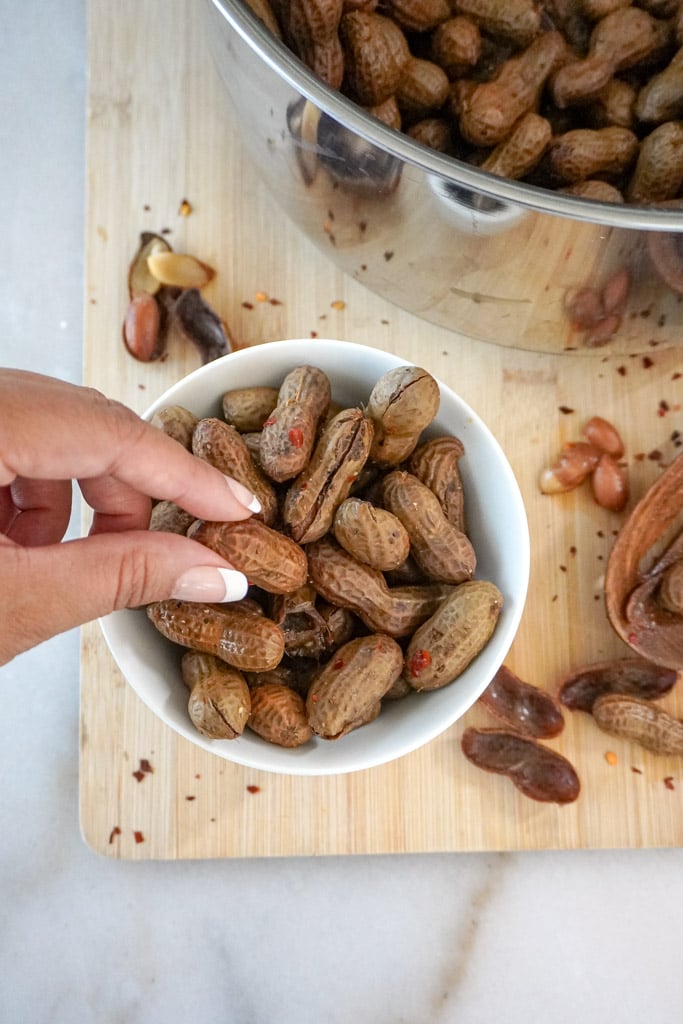 a hand reaching for one cajun boiled peanut in a small bowl