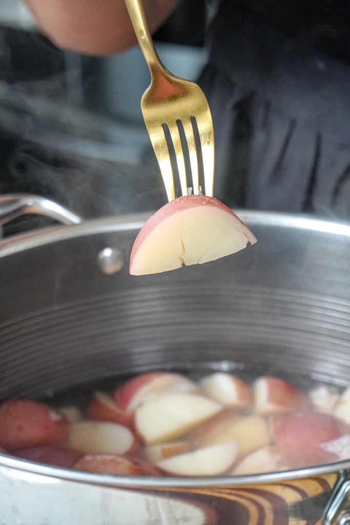 a fork inserted into a slice of red potato hovering over a pot
