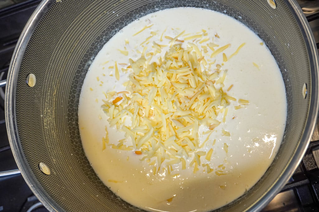 shredded cheese added to a pot of cream