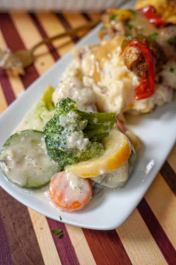 baked mixed vegetables on a plate with mashed potatoes and smothered chicken out of focus