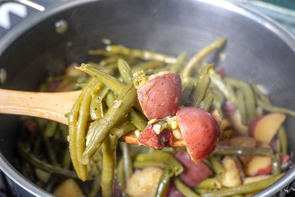 a wooden spoon holding smothered green beans over a pot containing more