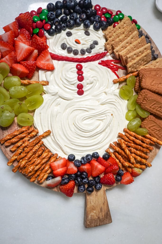 cheesecake dip shaped and decorated into a snowman adorned with fruit and cookies to dip into it