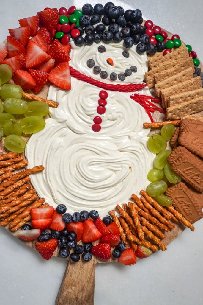 cheesecake dip shaped and decorated into a snowman adorned with fruit and cookies to dip into it