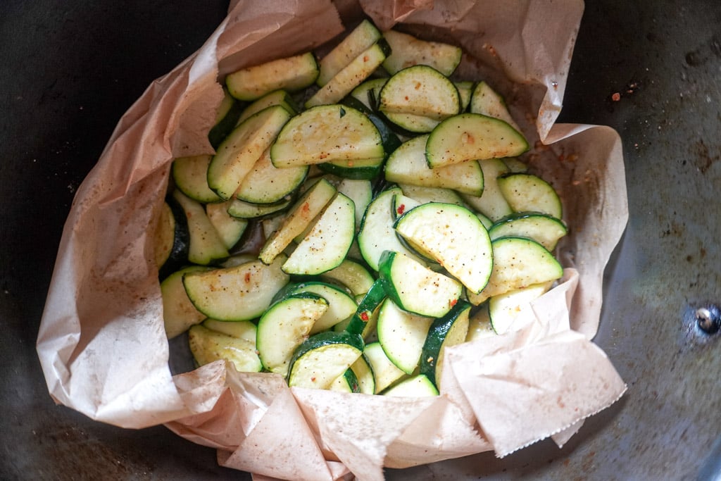 chopped and seasoned zucchini wrapped in parchment paper in an air fryer basket