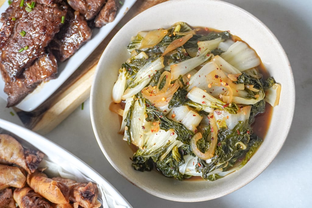 a bowl of baby bok choy beside other dishes