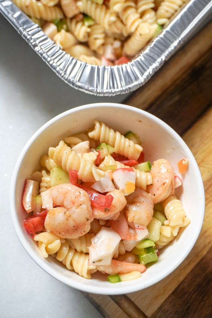 a bowl of seafood pasta salad beside a pan containing more