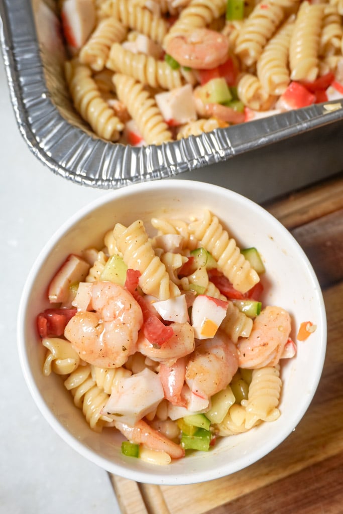 a bowl of seafood pasta salad beside a pan containing more