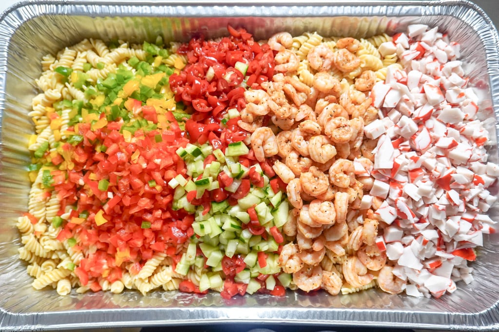 ingredients for a bowl of seafood pasta salad in a foil pan before mixing.