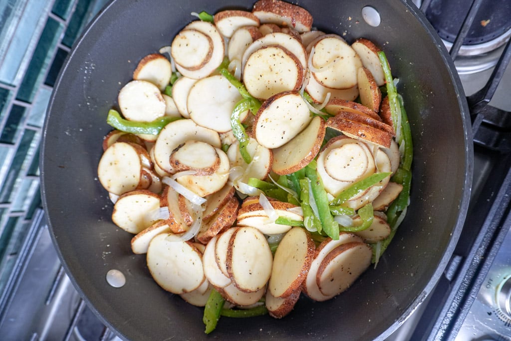 sliced potatoes added to skillet with sliced onions and peppers