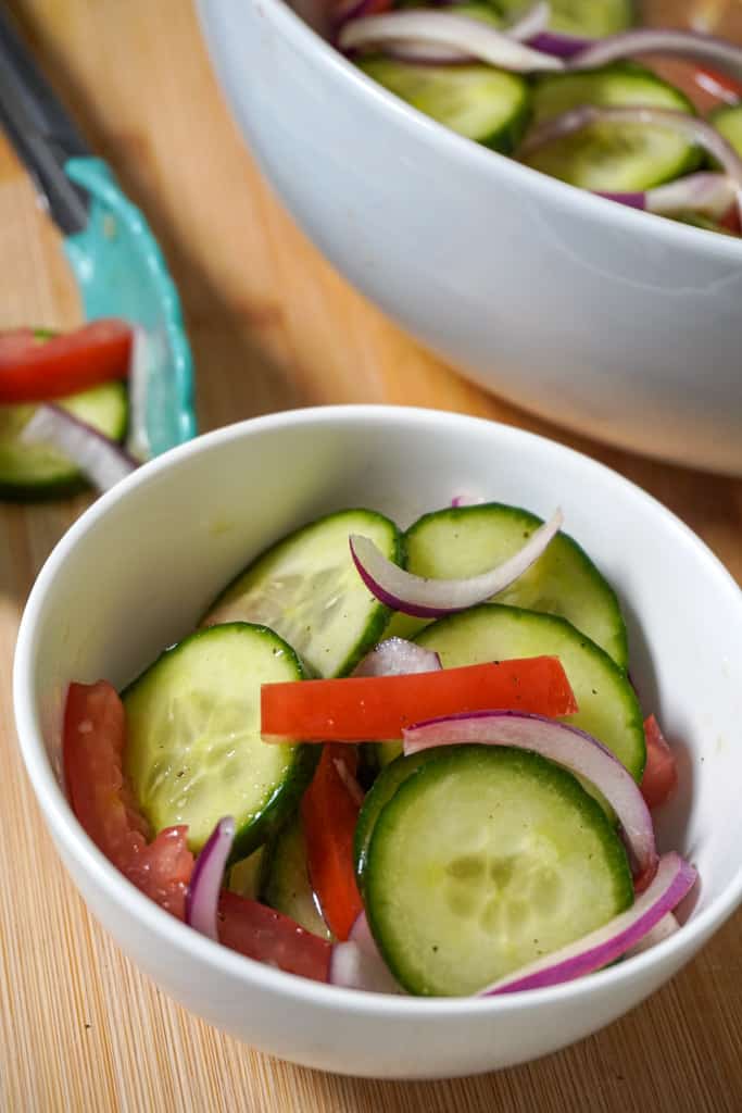 an individual serving of cucumber onion salad with a larger bowl in the background