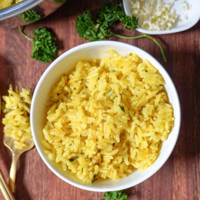 overhead view of a bowl of yellow greek rice next to a fork and scattered herbs