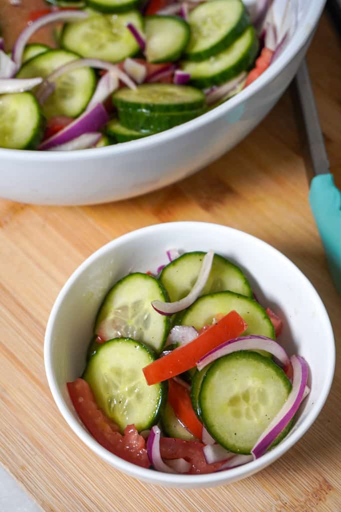 a small bowl of cucumber onion salad with a larger bowl containing more behind it