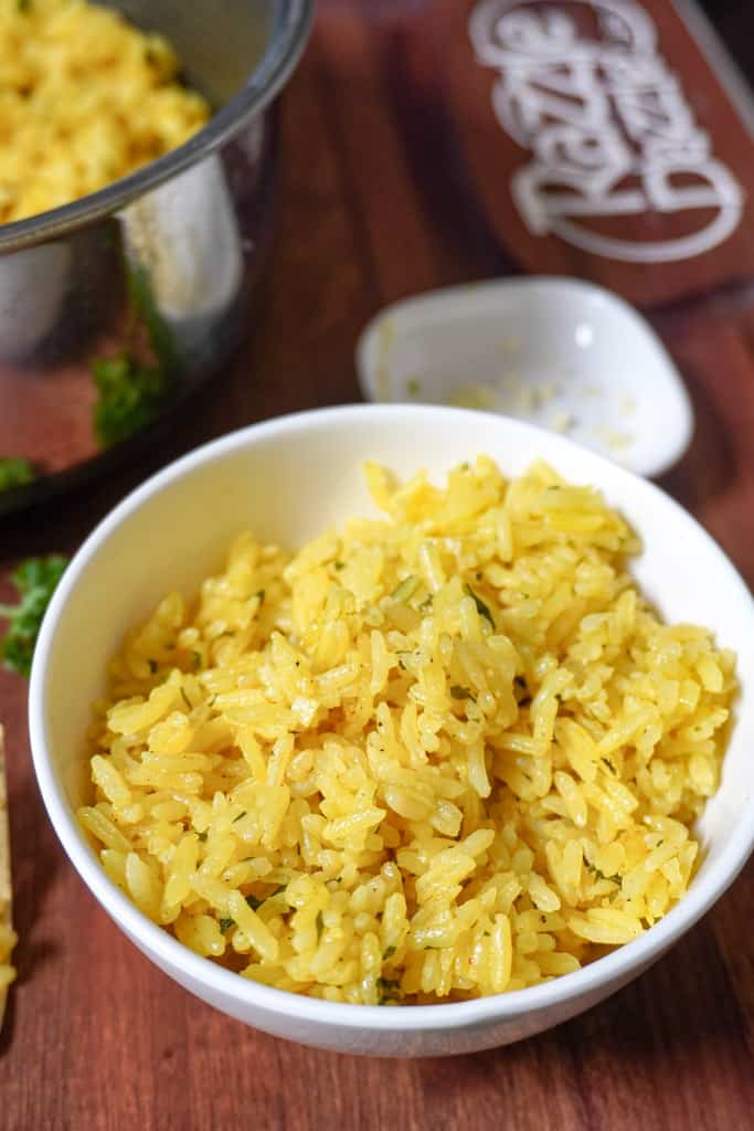 bowl of yellow Greek rice with a pot containing more in the background