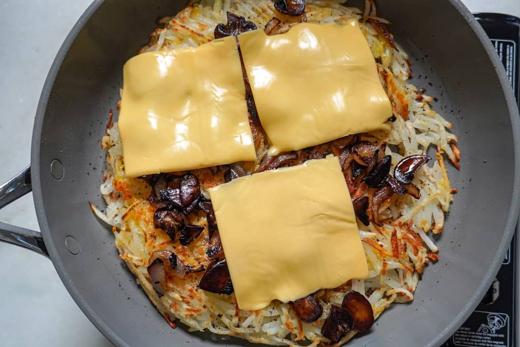 American cheese slices placed over shredded potatoes in skillet