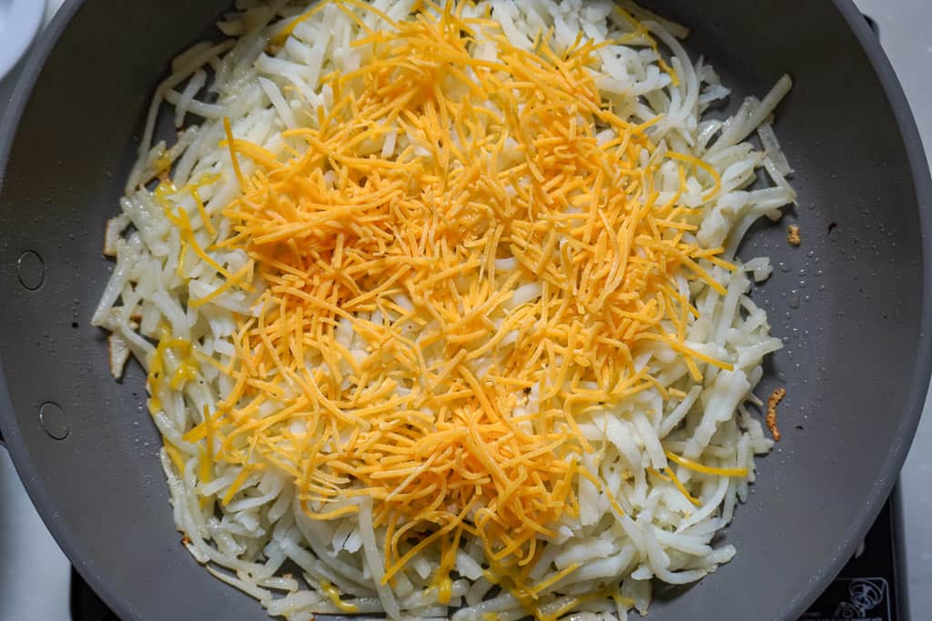 shredded cheese over potatoes in skillet