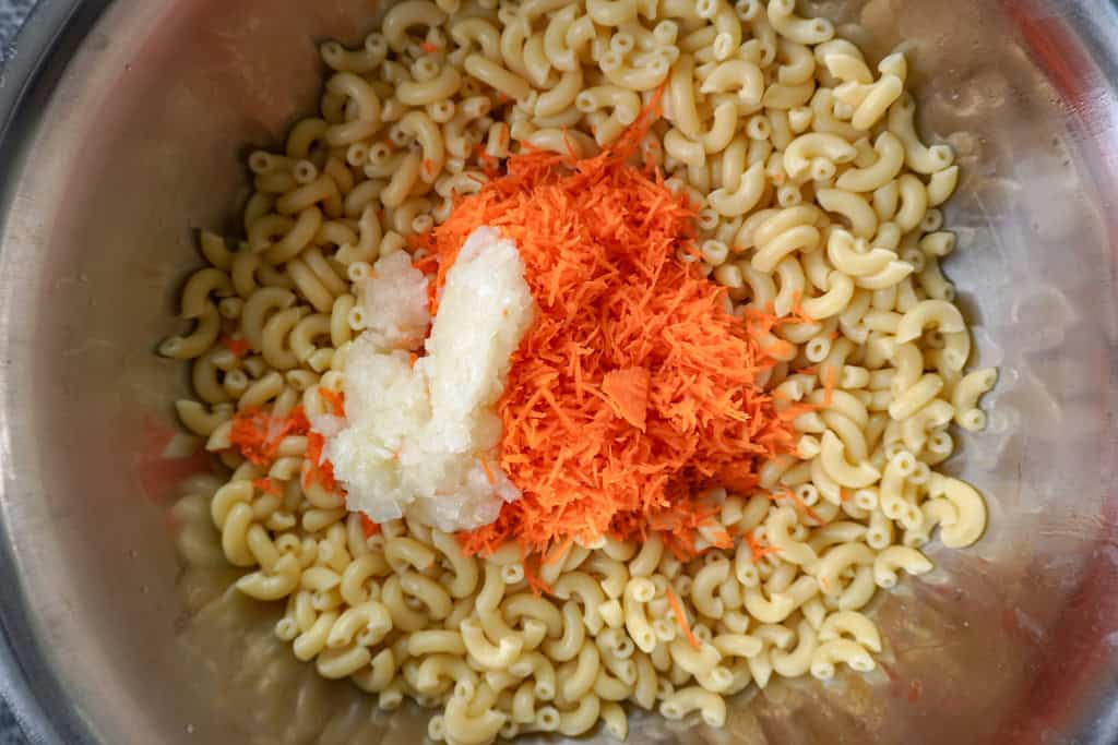 grated carrots ane onions added to bowl of cooked macaroni