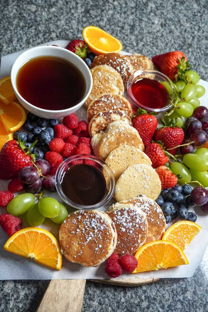 a fruit platter with pancakes and 3 syrups