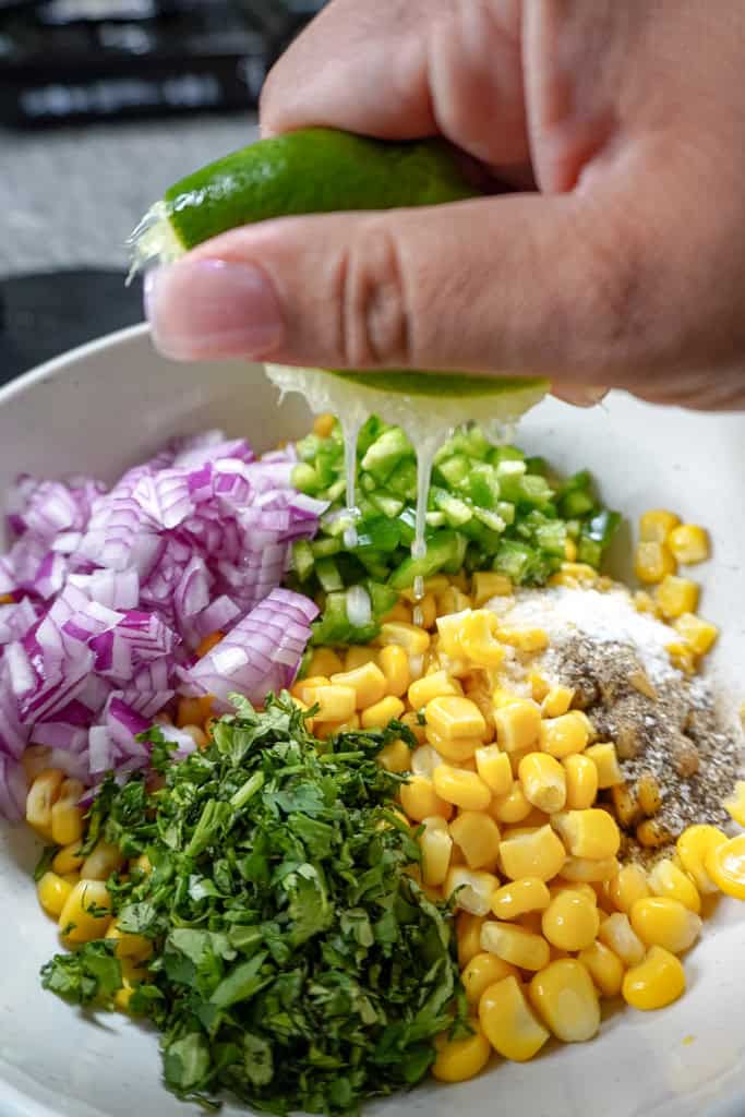 a hand squeezing lime juice over fresh salsa ingredients
