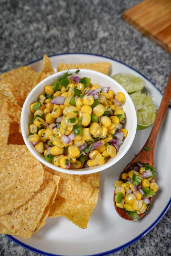 a bowl of Chipotle corn salsa on a platter with tortilla chips and sliced lime