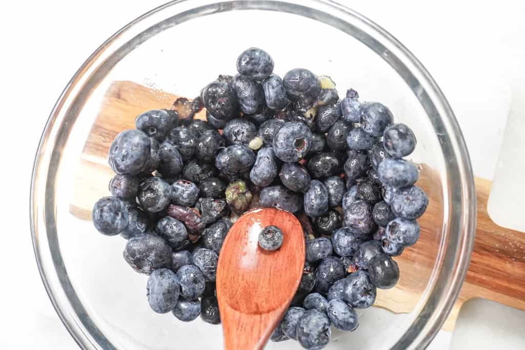 Fresh blueberries in a glass bowl with a wooden spoon.