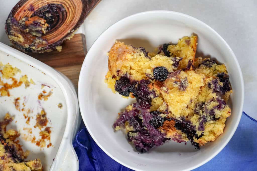 A bowl of blueberry cobbler next to the nearly empty baking dish.