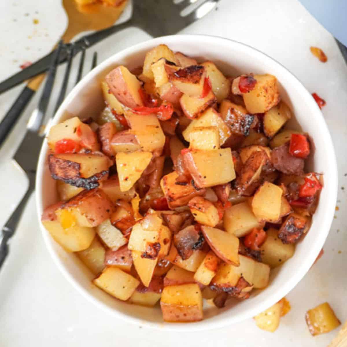 A bowl of cooked Potatoes O'Brien with diced red and yellow bell peppers and onions.