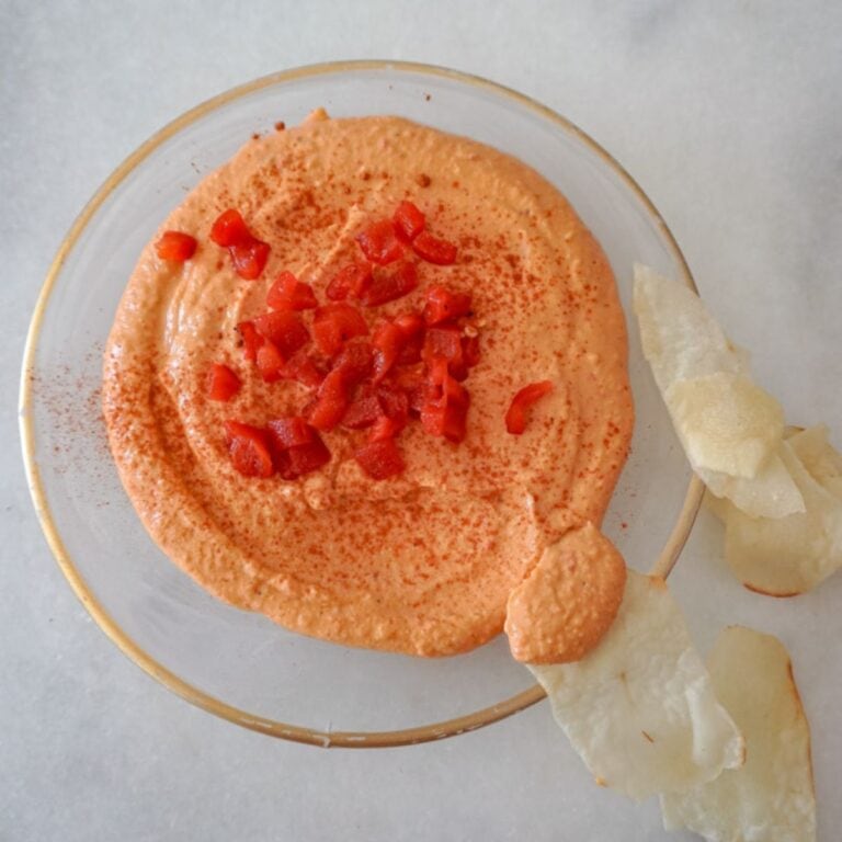 overhead view of roasted red pepper hummus in a saucer with chips scattered around