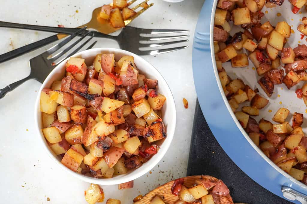 Overhead shot of a bowl of Potatoes O'Brien with forks and a skillet in the background.