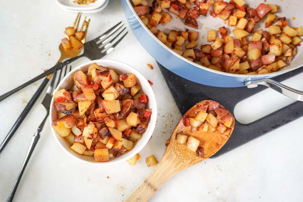 A bowl of Potatoes O'Brien next to a skillet with remaining potatoes.