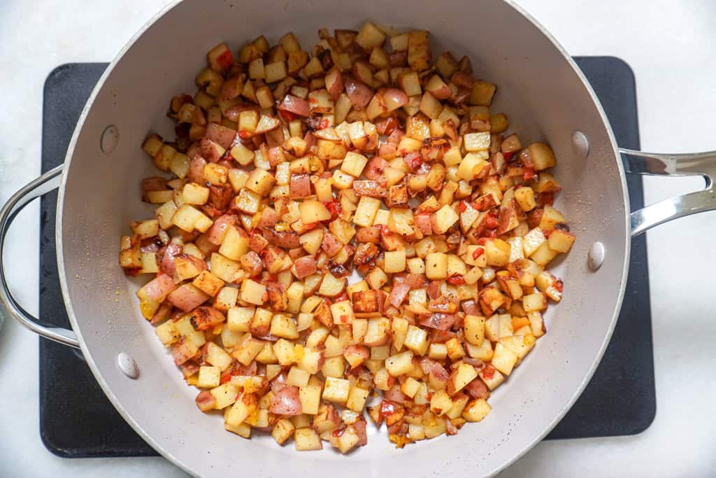 Diced potatoes, red and yellow bell peppers, and onions cooking in a large skillet.