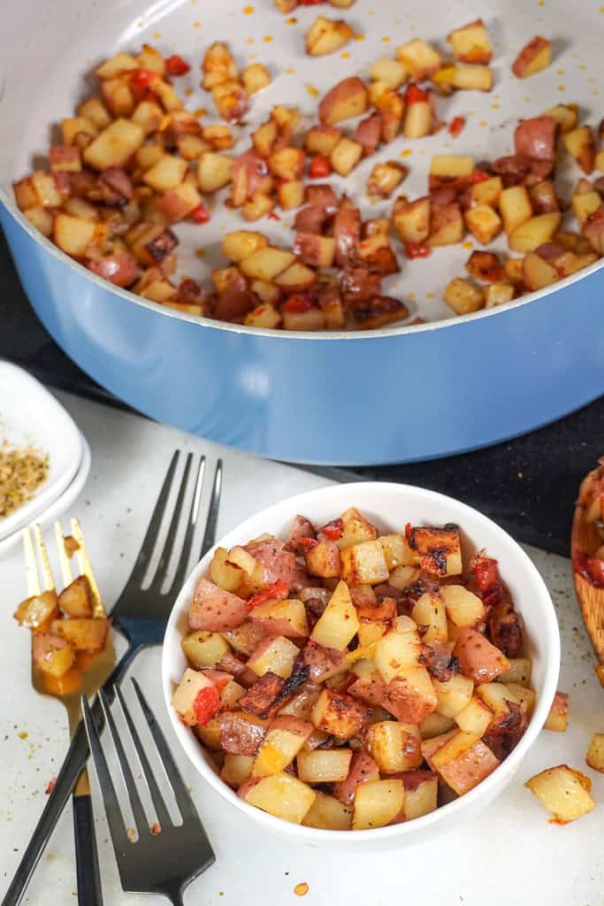 A bowl of Potatoes O'Brien next to a skillet with remaining potatoes.