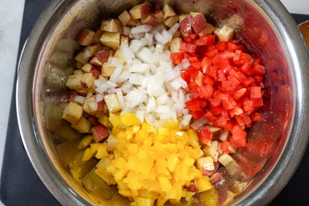 Diced potatoes, red and yellow bell peppers, and onions cooking in a large skillet.