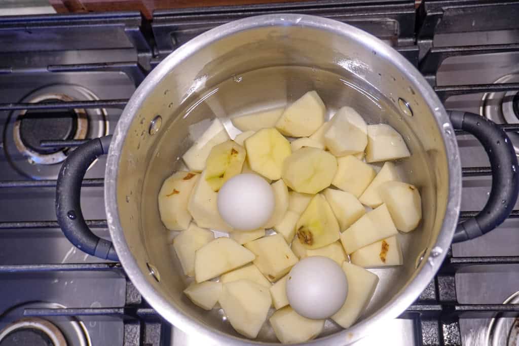 overhead view of diced potatoes and two large eggs in a pot filled with water