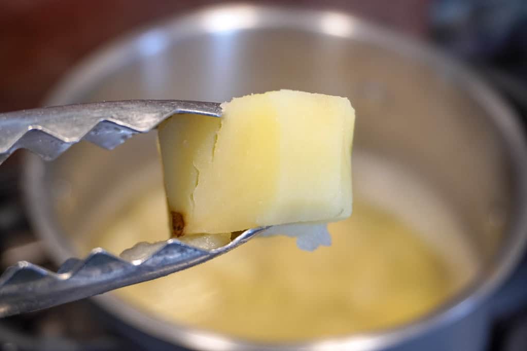 a tong holding a cubed boiled potato over a pot