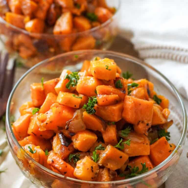 A close-up of sweet potato hash served in a glass bowl, highlighting caramelized edges and garnished with parsley.