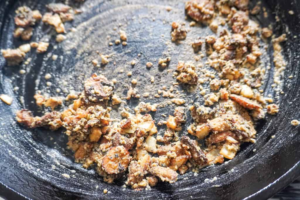 Lightly browned flour-coated onion and mushroom bits scattered in a cast-iron skillet.