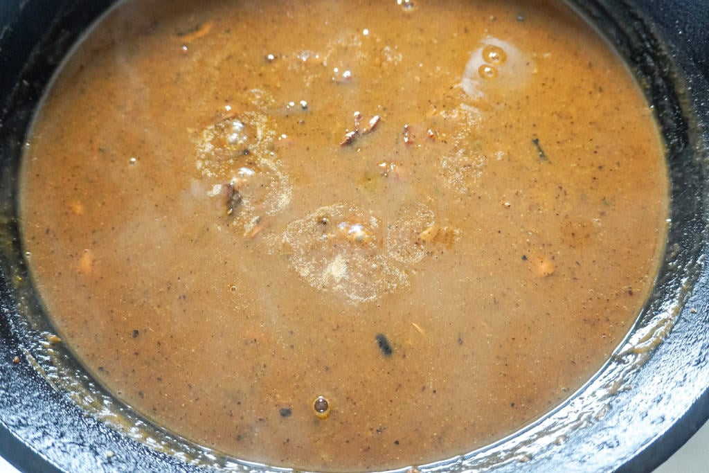 Simmering brown gravy with flecks of seasoning and caramelized bits in a cast-iron skillet.