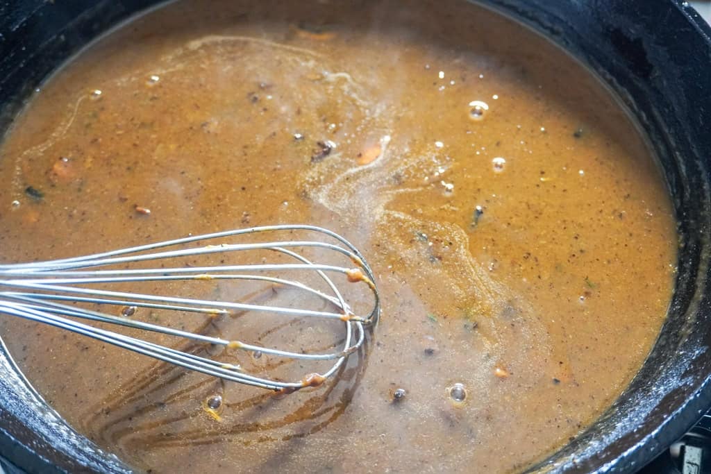 A metal whisk stirring a smooth, glossy brown gravy in a cast-iron skillet.