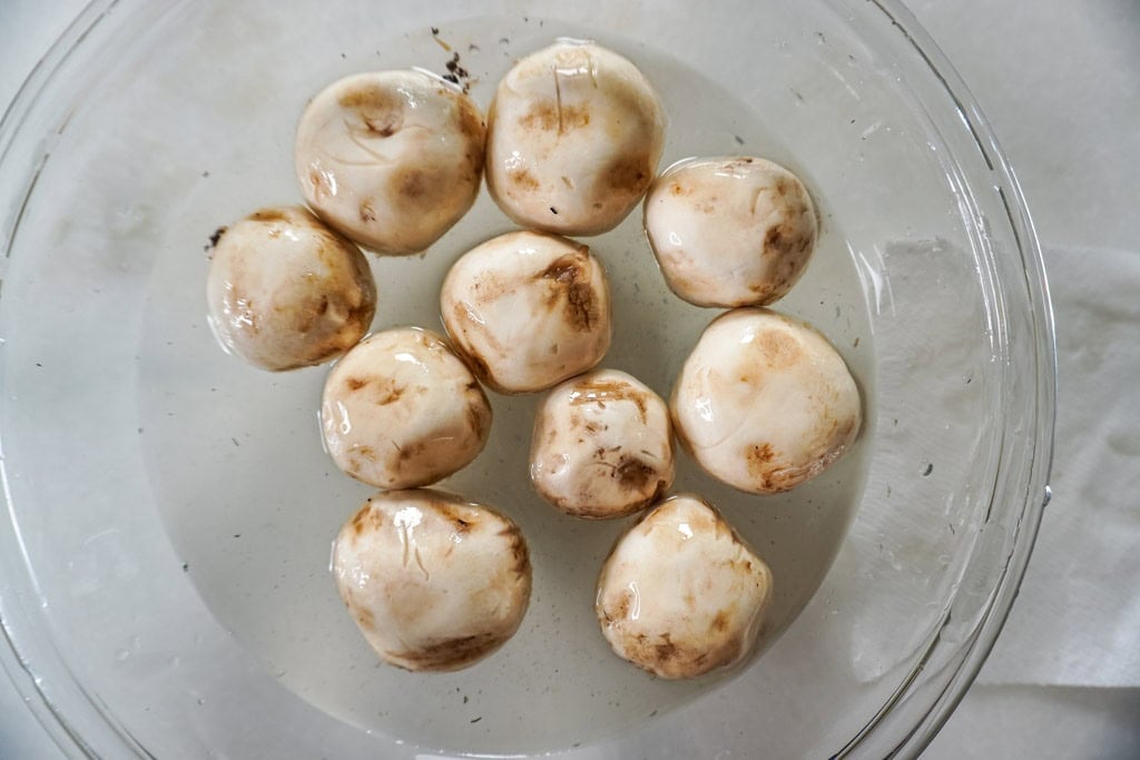 A glass bowl filled with water where mushrooms are being washed, with dirt visibly floating in the water.