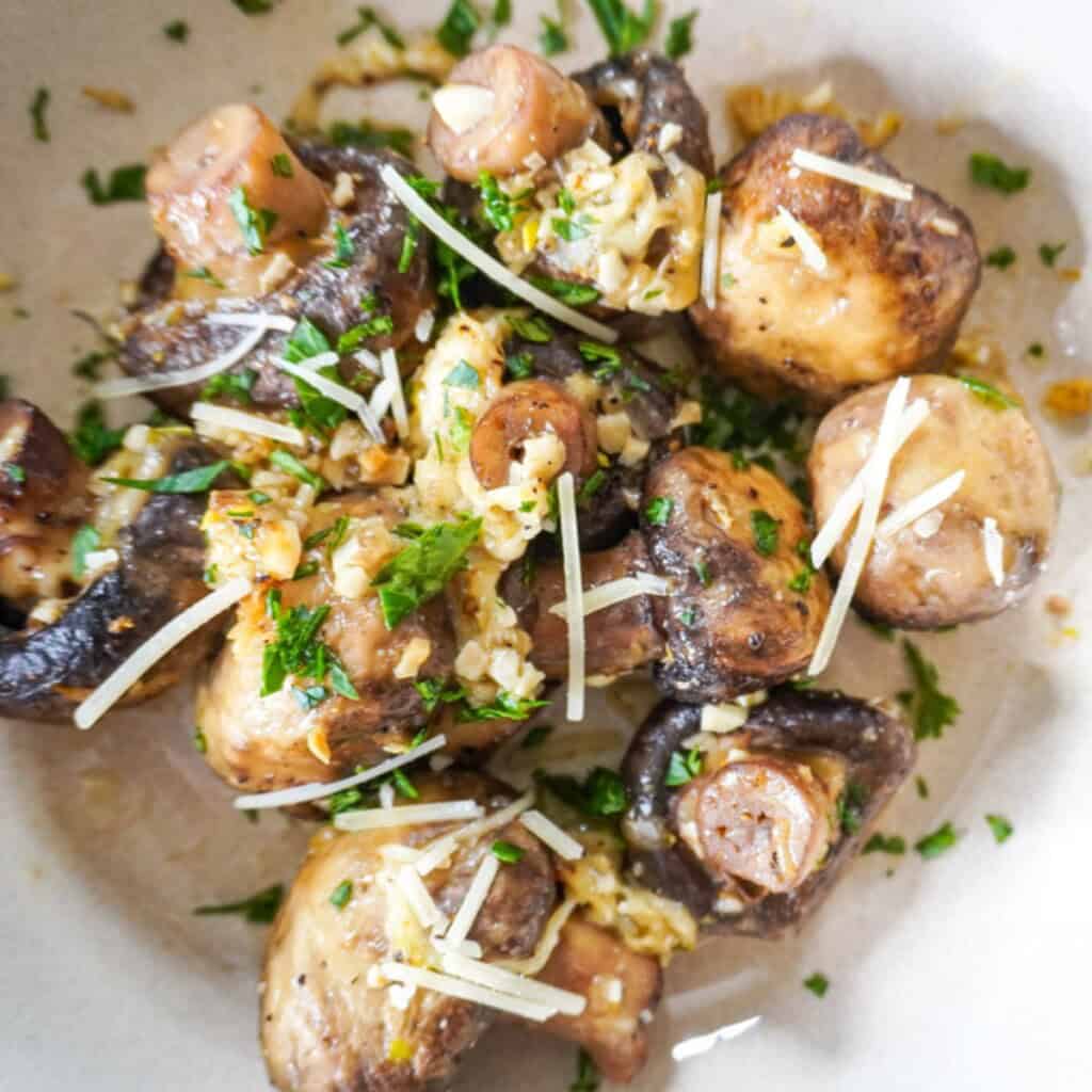 A close-up of golden air-fried mushrooms glistening with garlic butter, Parmesan, and fresh herbs, with strands of cheese melting over the surface.