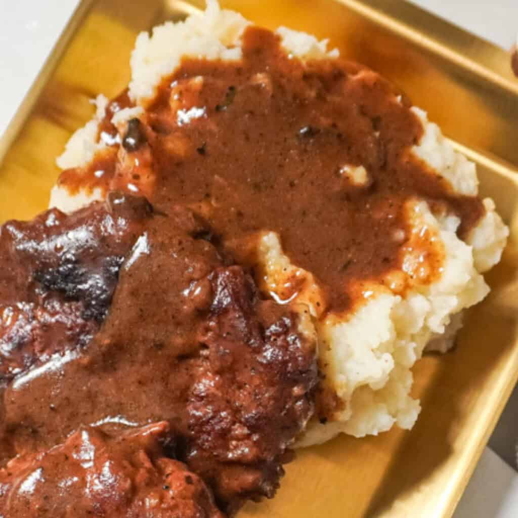 Close-up of creamy mashed potatoes topped with rich brown gravy, served alongside a juicy hamburger steak on a gold tray.