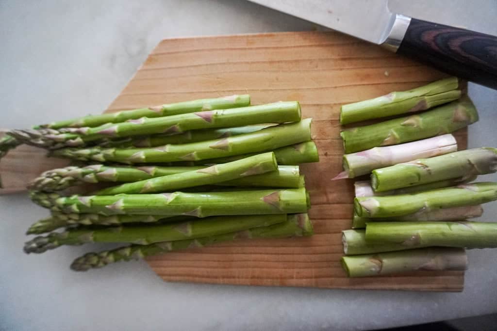A cutting board with fresh asparagus, neatly trimmed to remove the woody ends, with a knife placed beside them.